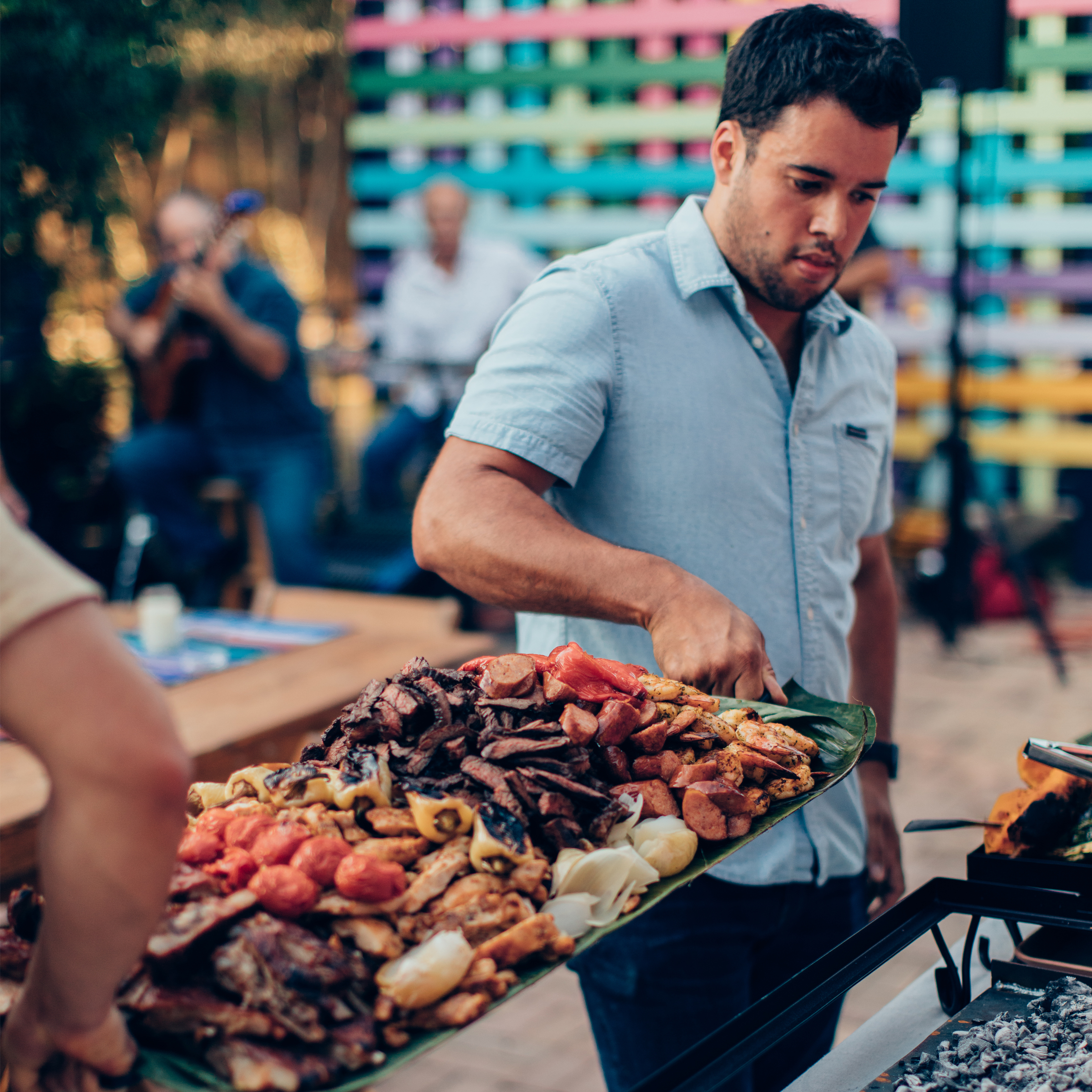 Man serving a large platter of grilled asada meats outdoors at a Siete headquarters event