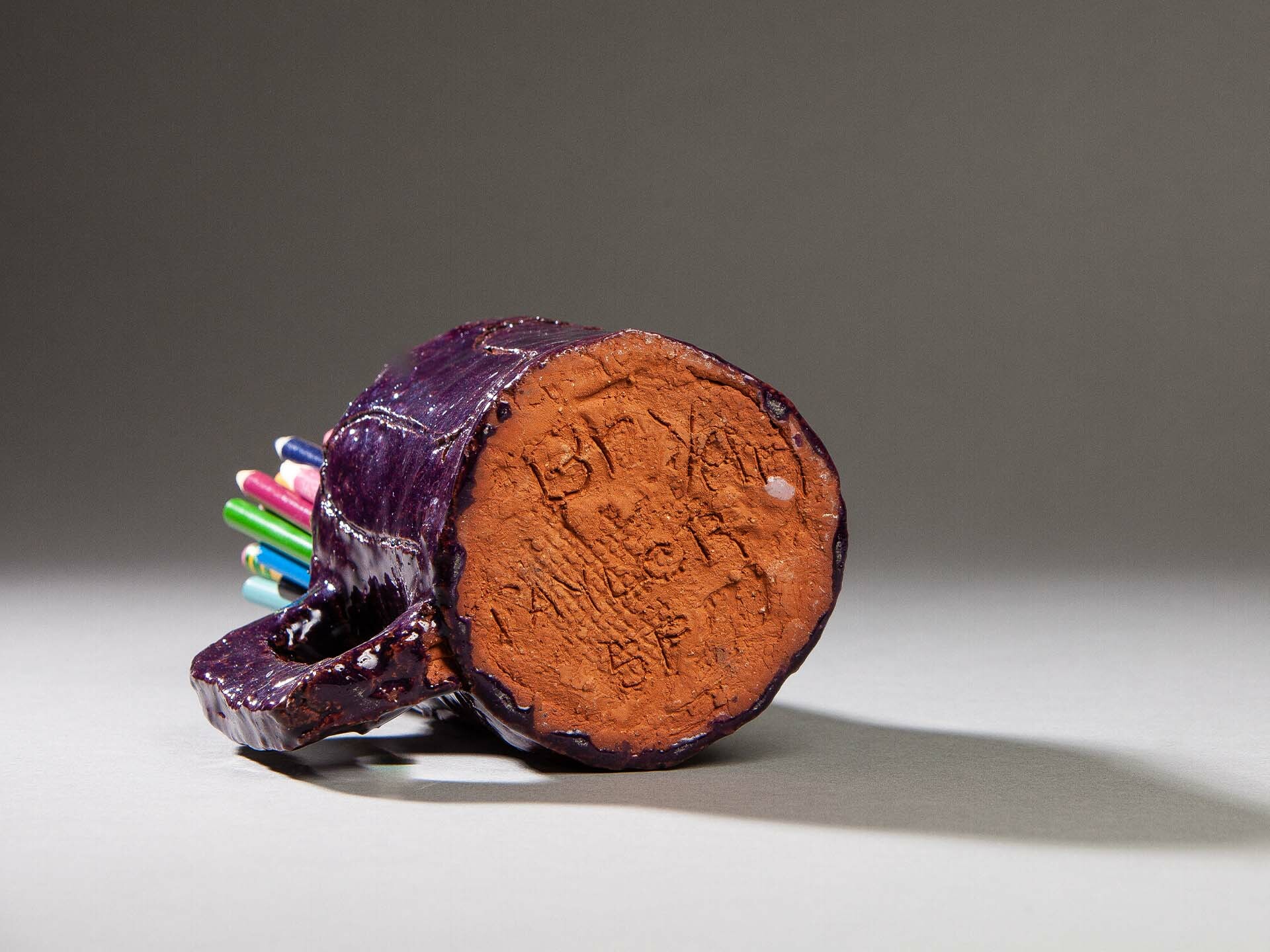 Handmade purple mug tipped to show its unglazed terracotta base with scratched marks