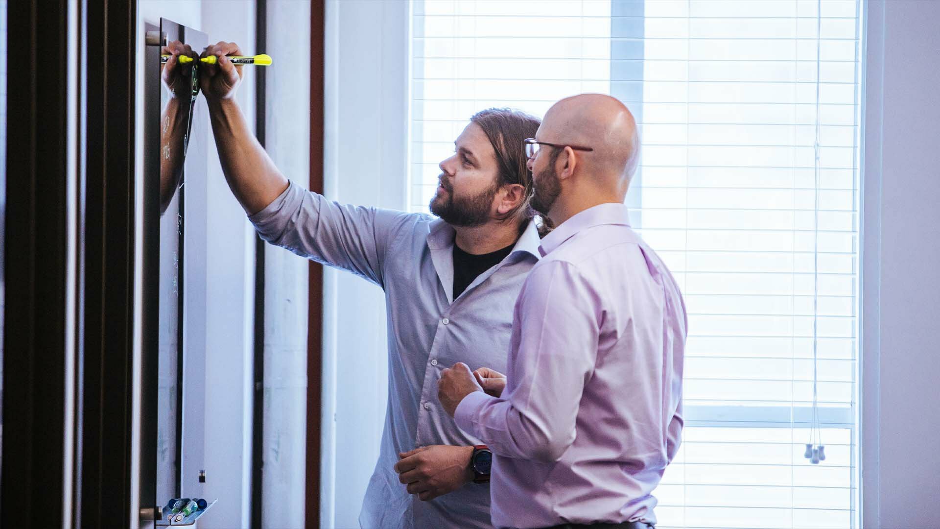 Two men measuring and marking a wall with a level during a workspace buildout
