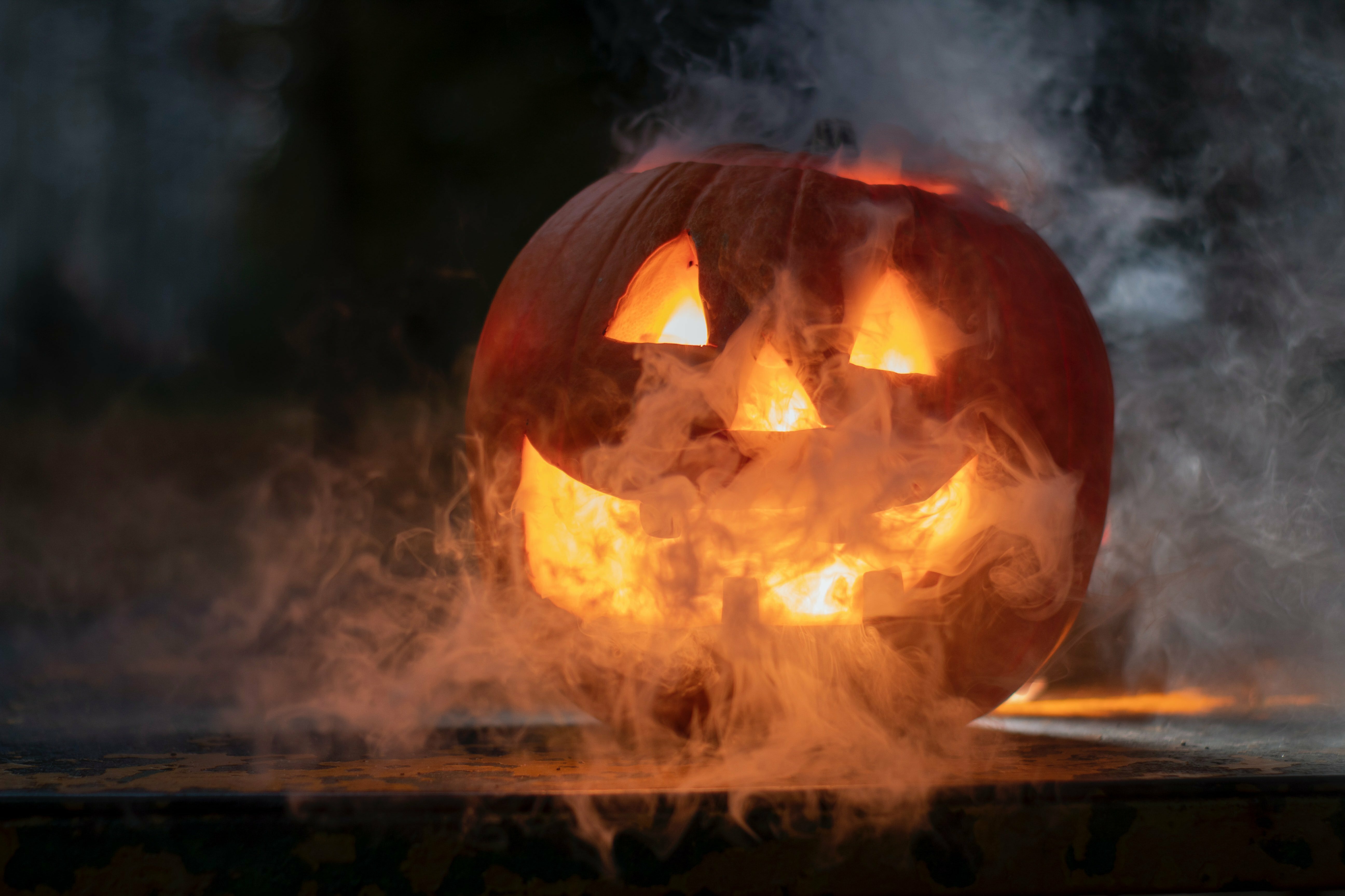 Glowing carved jack-o'-lantern smiling through swirling smoke in the dark