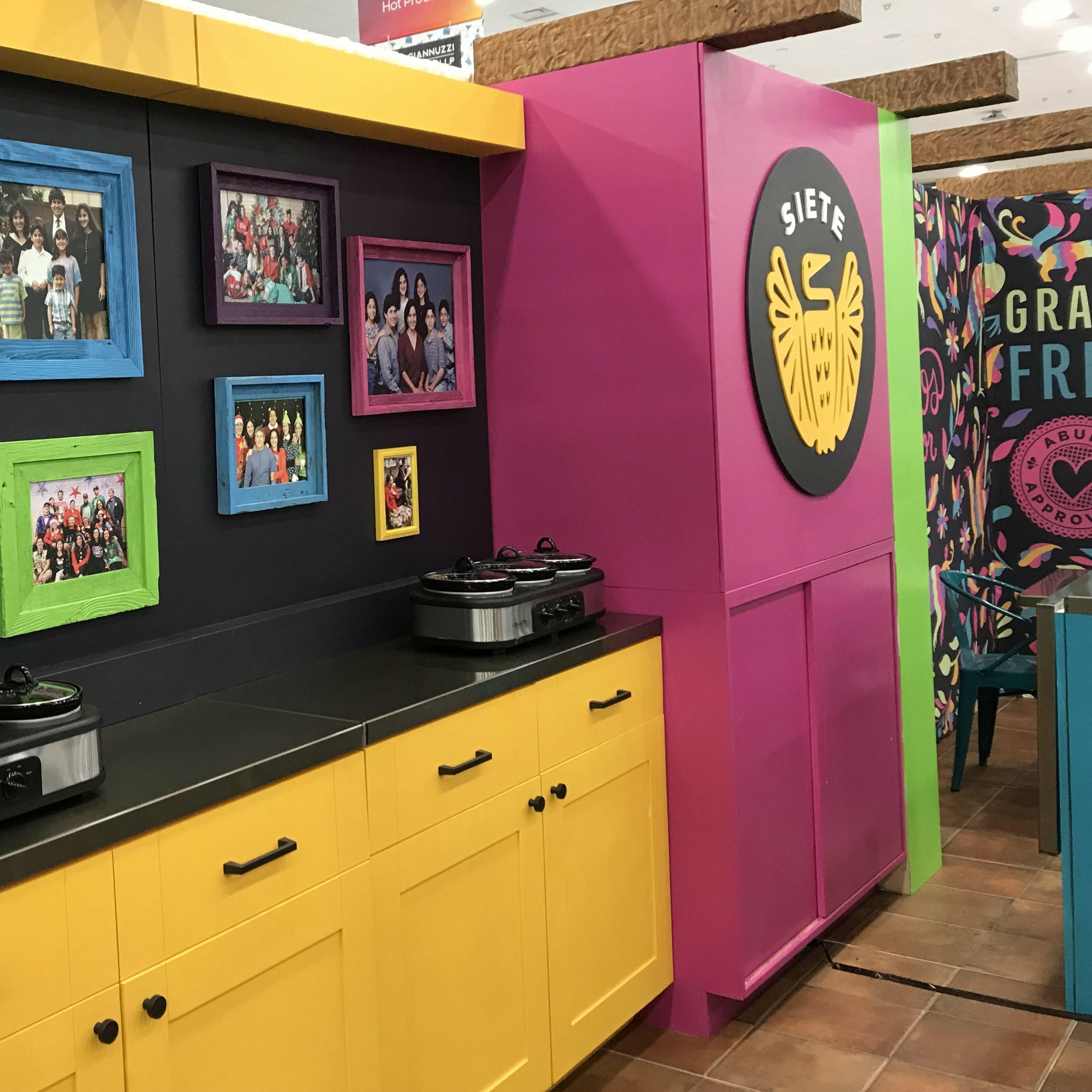 Siete booth kitchen with yellow cabinets, slow cookers and family photos beside Siete logo