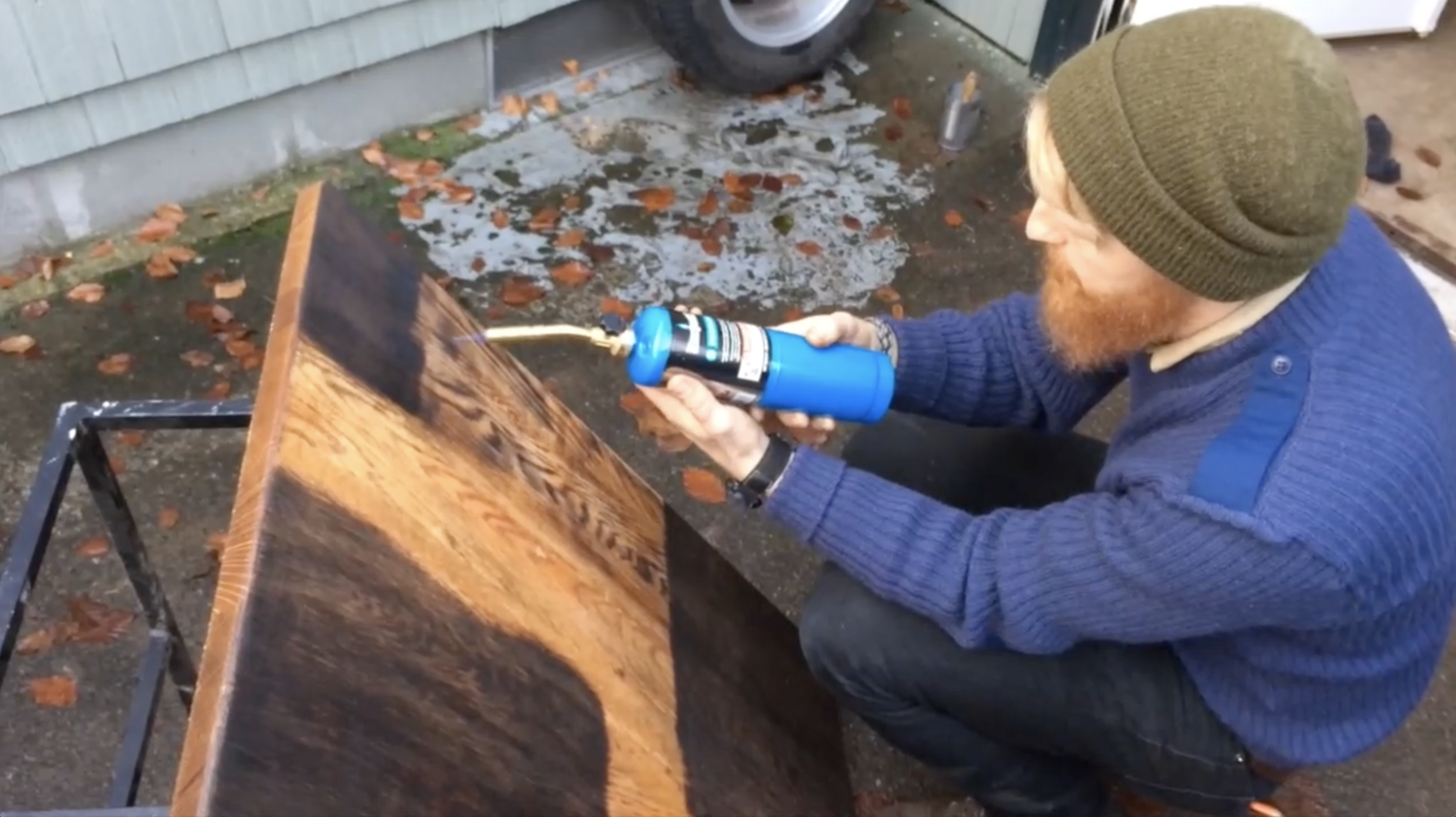 Bearded man in a beanie applying finish to a live-edge wood slab outdoors