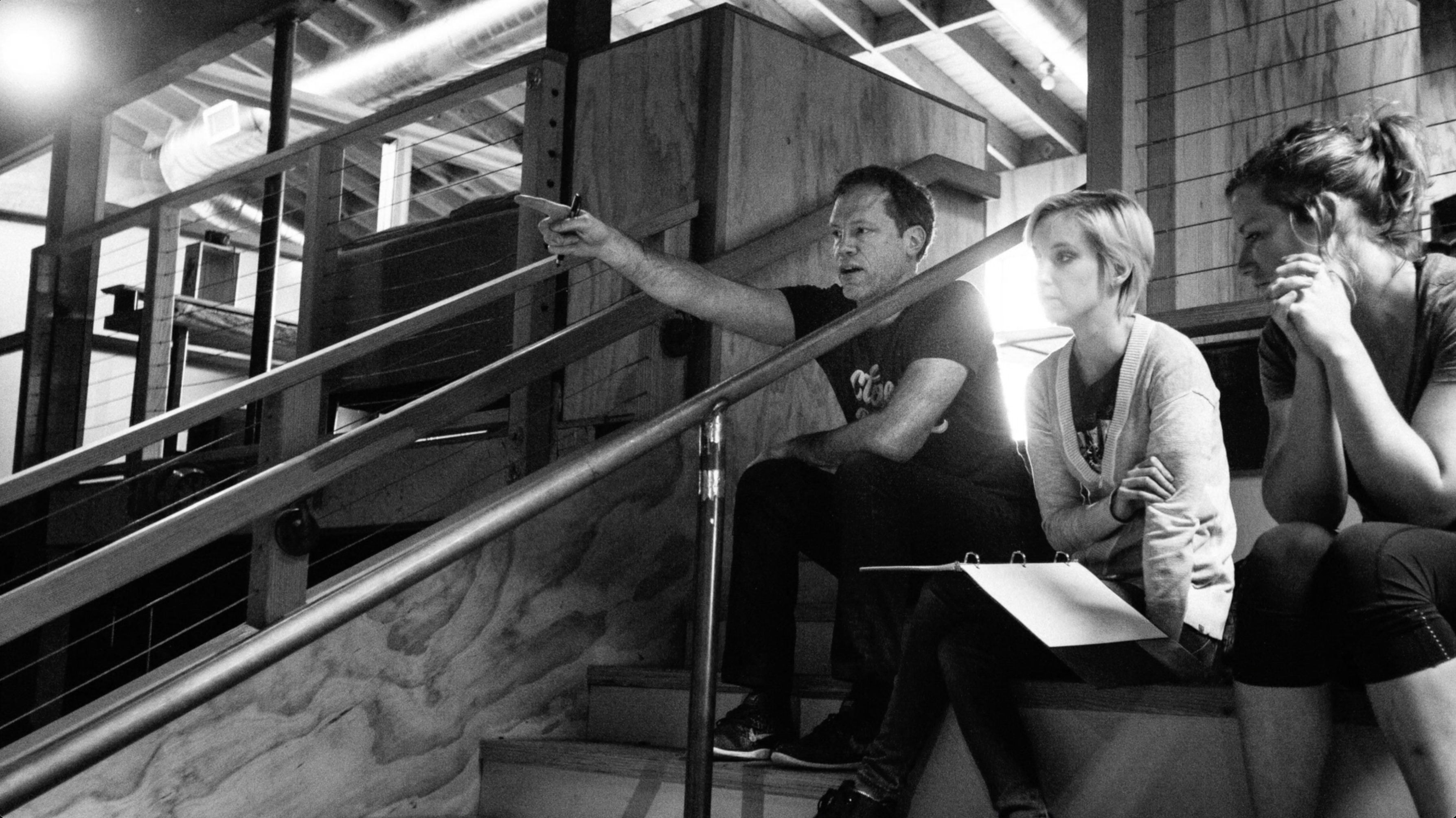 Three people in discussion on stairs reviewing a clipboard, black-and-white