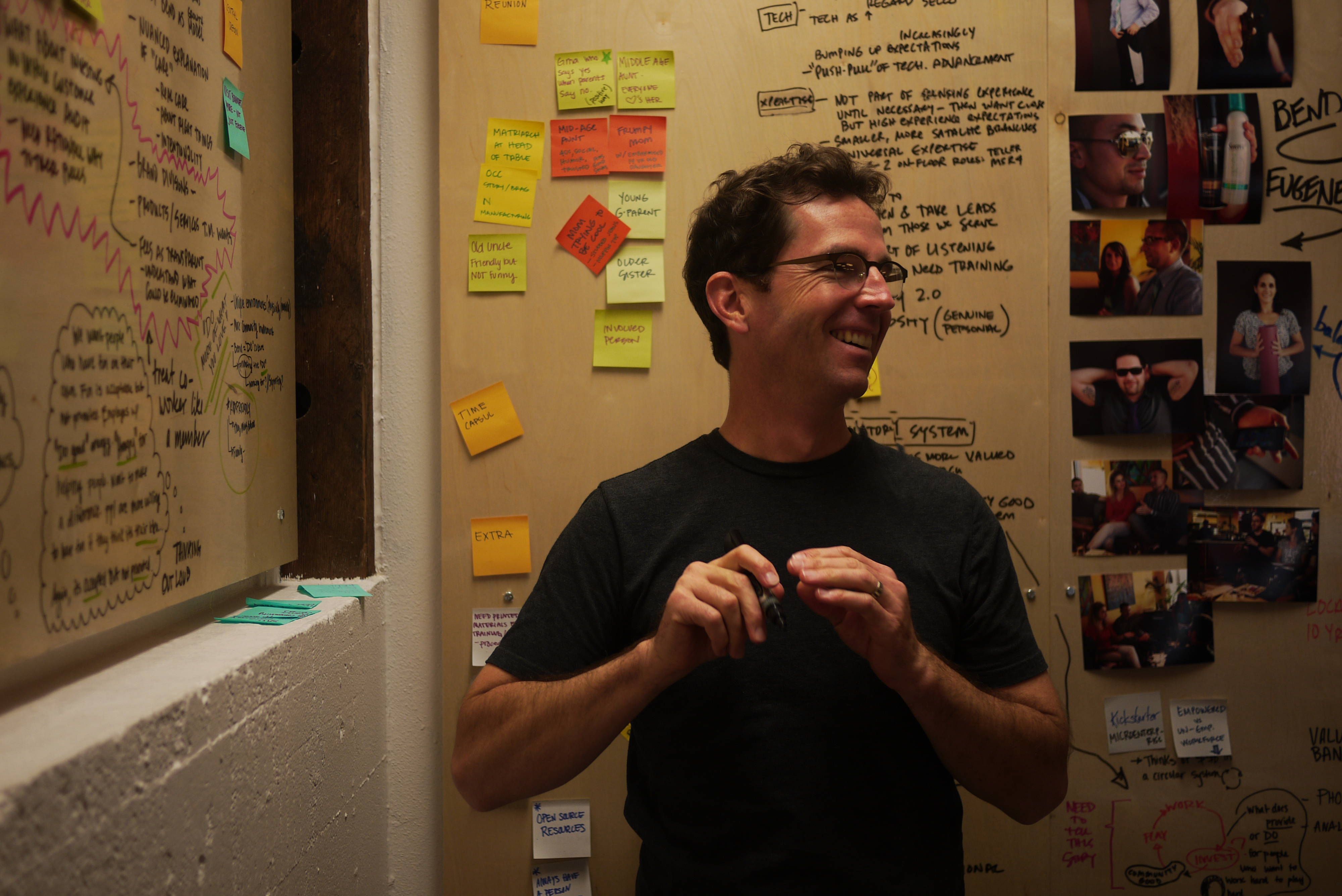 Smiling man at a brainstorm wall covered in handwritten notes and sticky notes