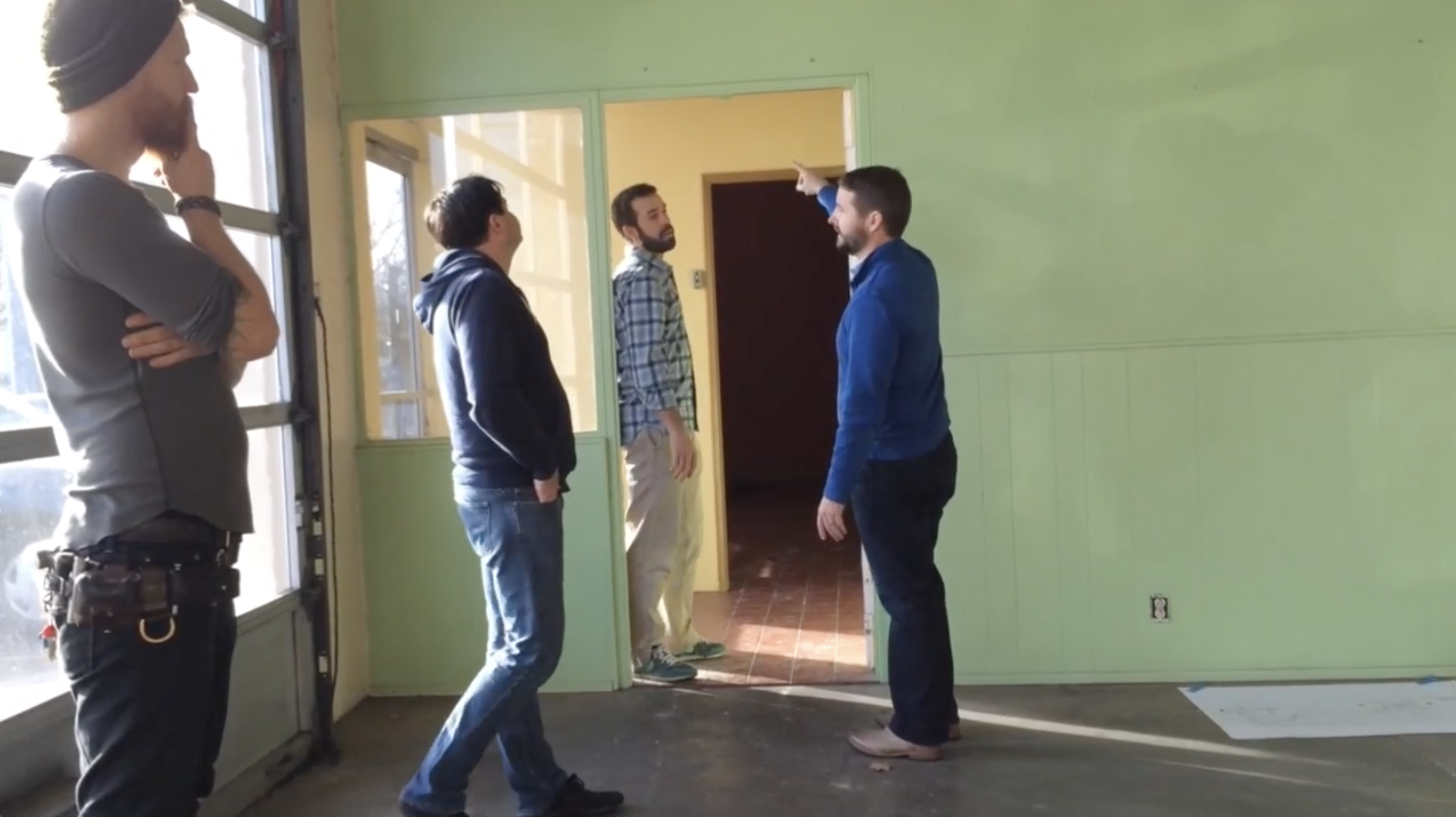 Four people surveying an empty green-walled room during a site walkthrough