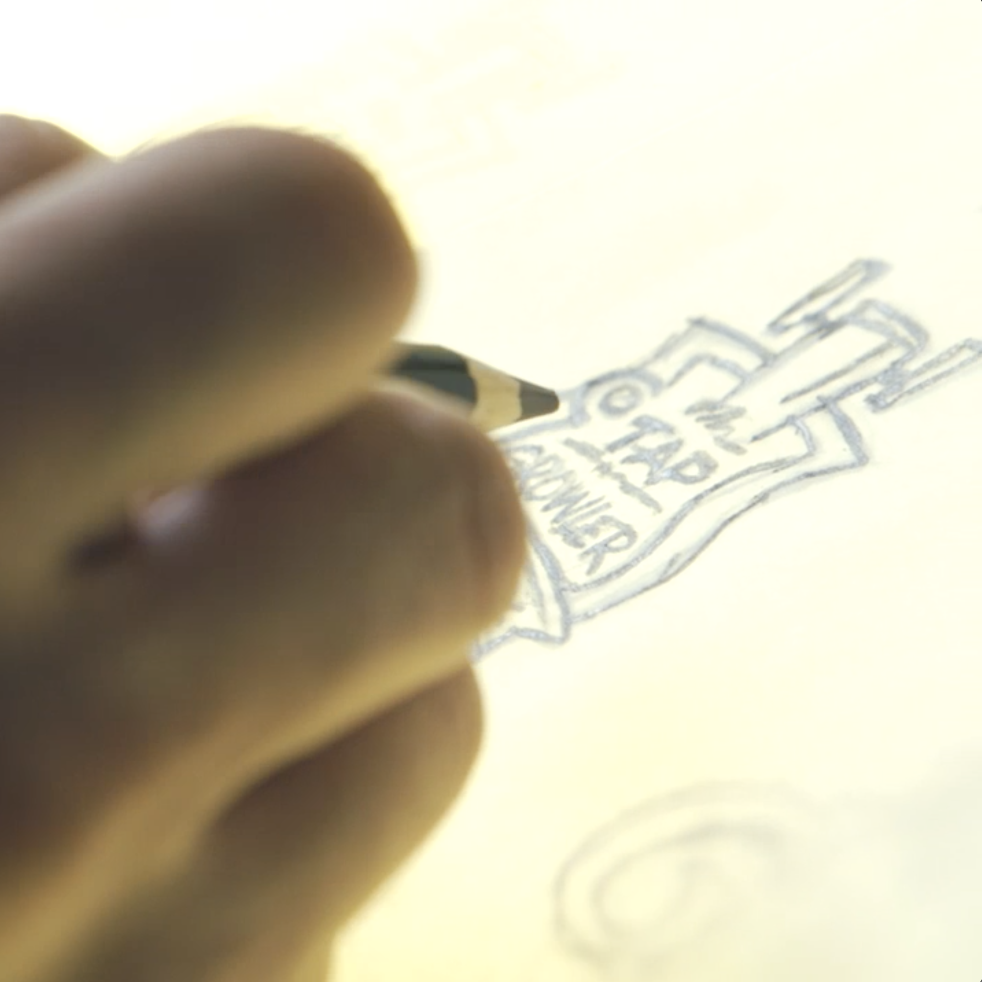 Hand sketching a logo design in pencil on bright backlit paper