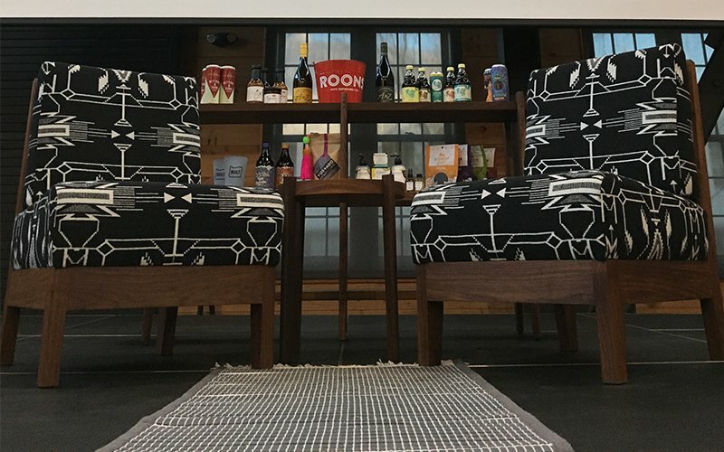 Two patterned black-and-white lounge chairs flanking a shelf of bottled drinks, set for fireside chats