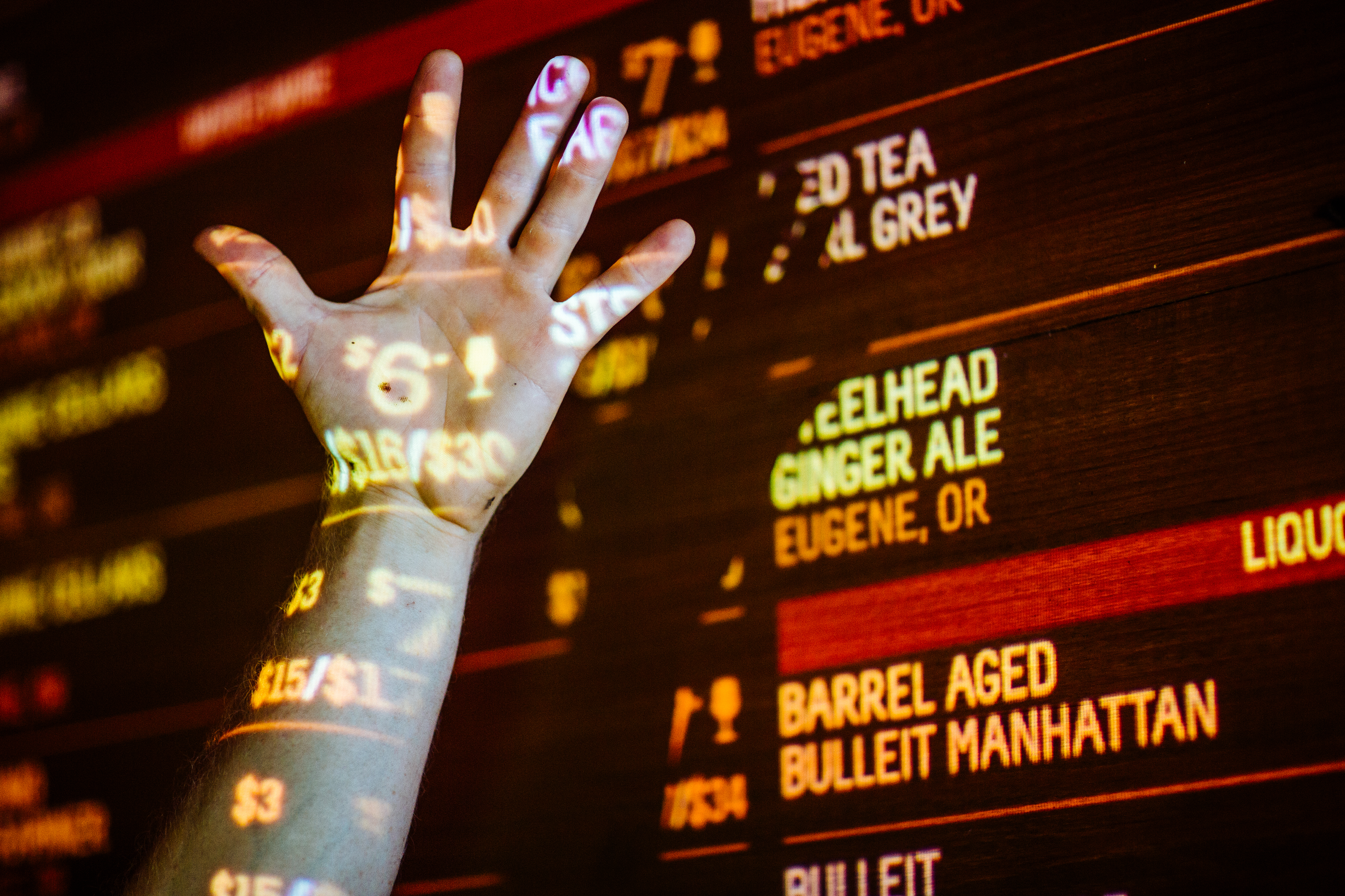 Hand raised against an illuminated draft beer menu board listing taps and prices at Beergarden food hall