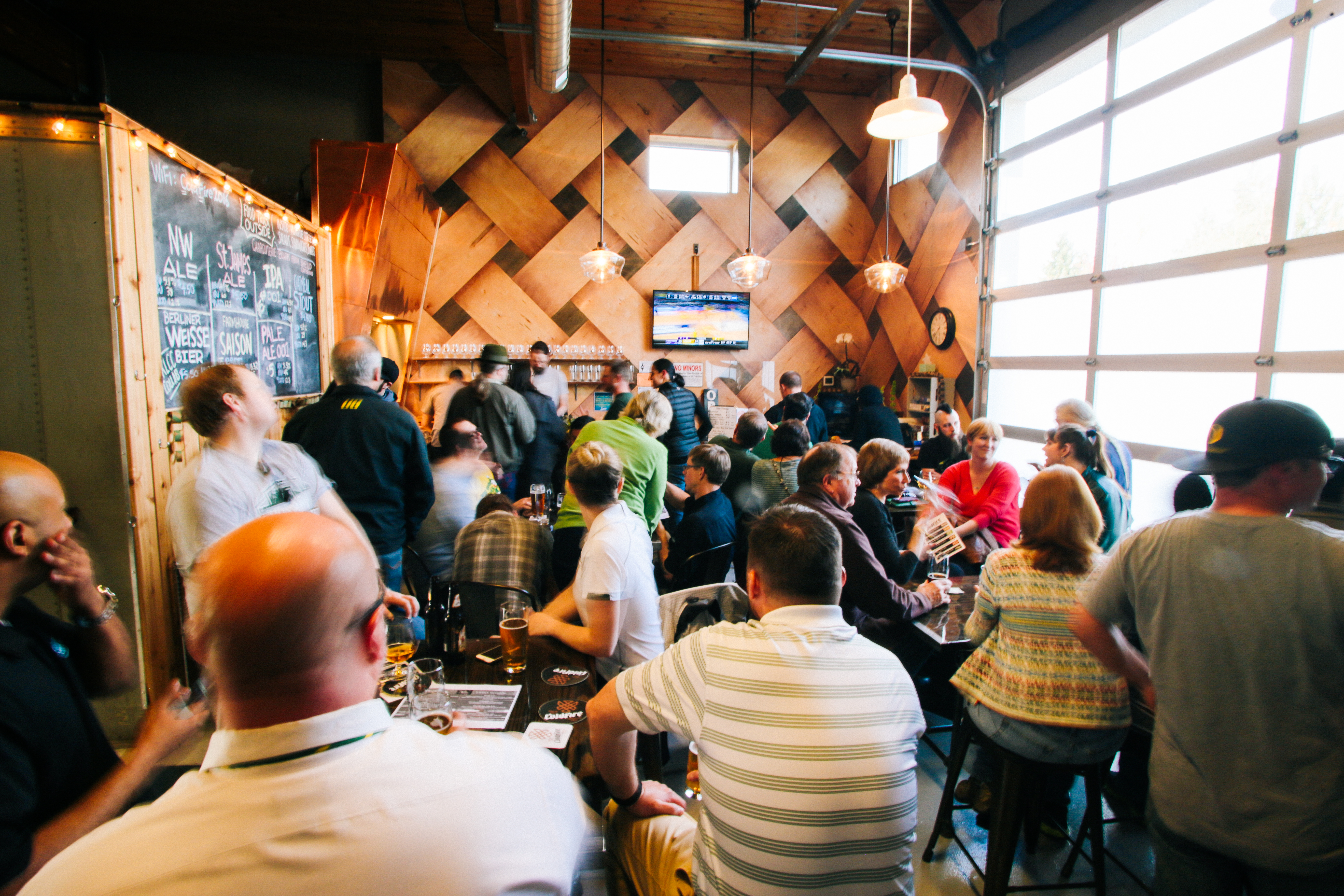 Completed ColdFire taproom packed with patrons beneath the diamond wood feature wall and a wall TV
