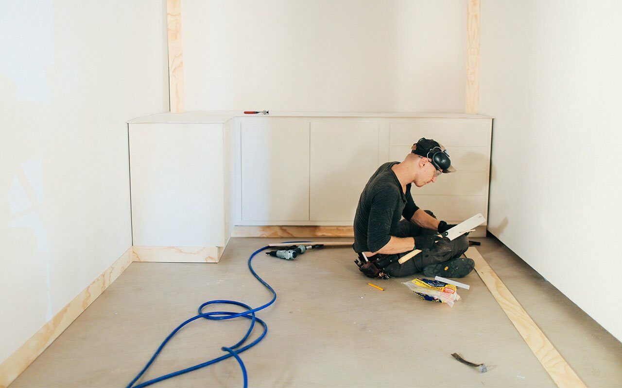 Worker in a headlamp kneeling to install white cabinets in an unfinished room