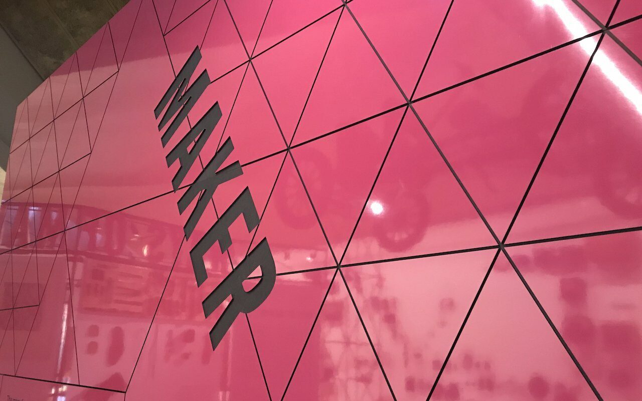 Pink triangulated glass wall with the word 'MAKER' in dark vertical lettering