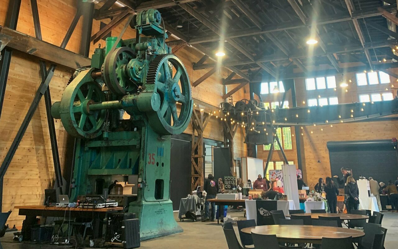 Vintage green industrial press machine inside the timber-framed Built Oregon Festival venue with string lights