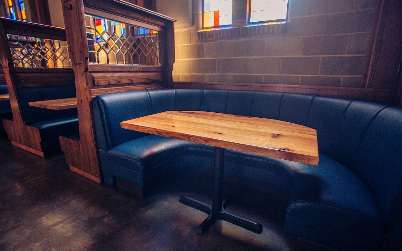 Curved blue leather banquette with live-edge wood table and stained-glass windows in a Drawn-designed interior