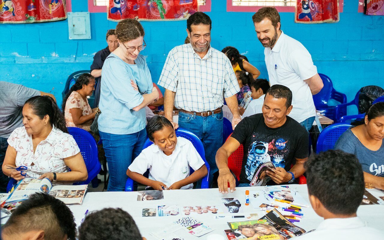 Drawn team members and locals making collages together at tables in a blue El Salvador classroom