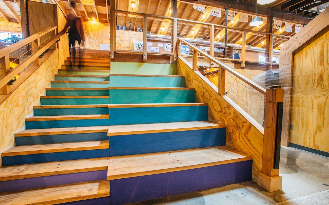 Person climbing colorful painted staircase in Drawn's Bard with timber beams and cable railings