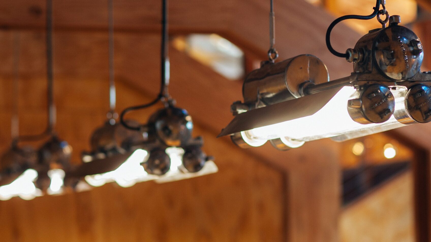 Row of vintage industrial pendant tube lights hanging against warm wood paneling