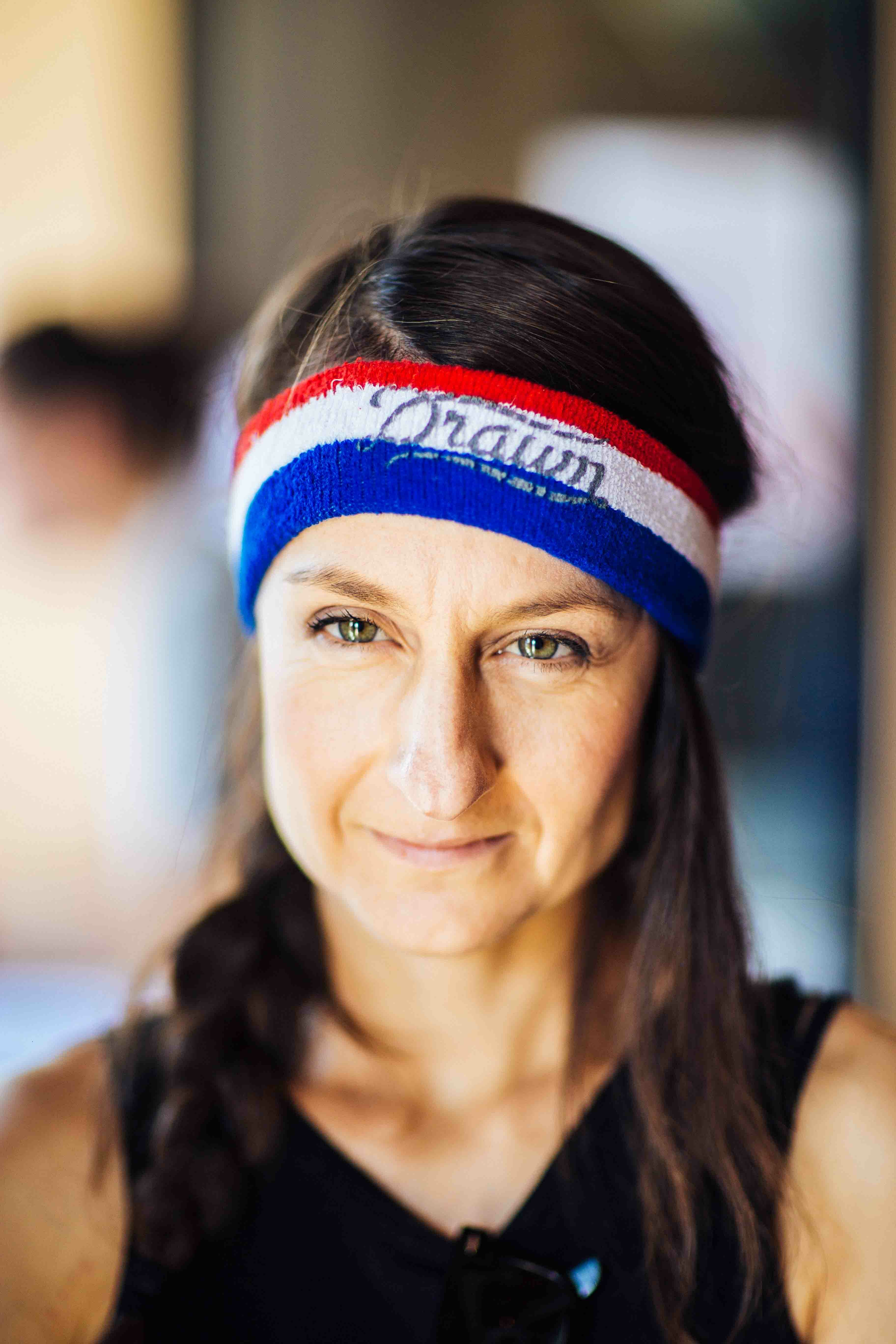 Woman wearing a red, white and blue Drawn sweatband, smiling at the camera