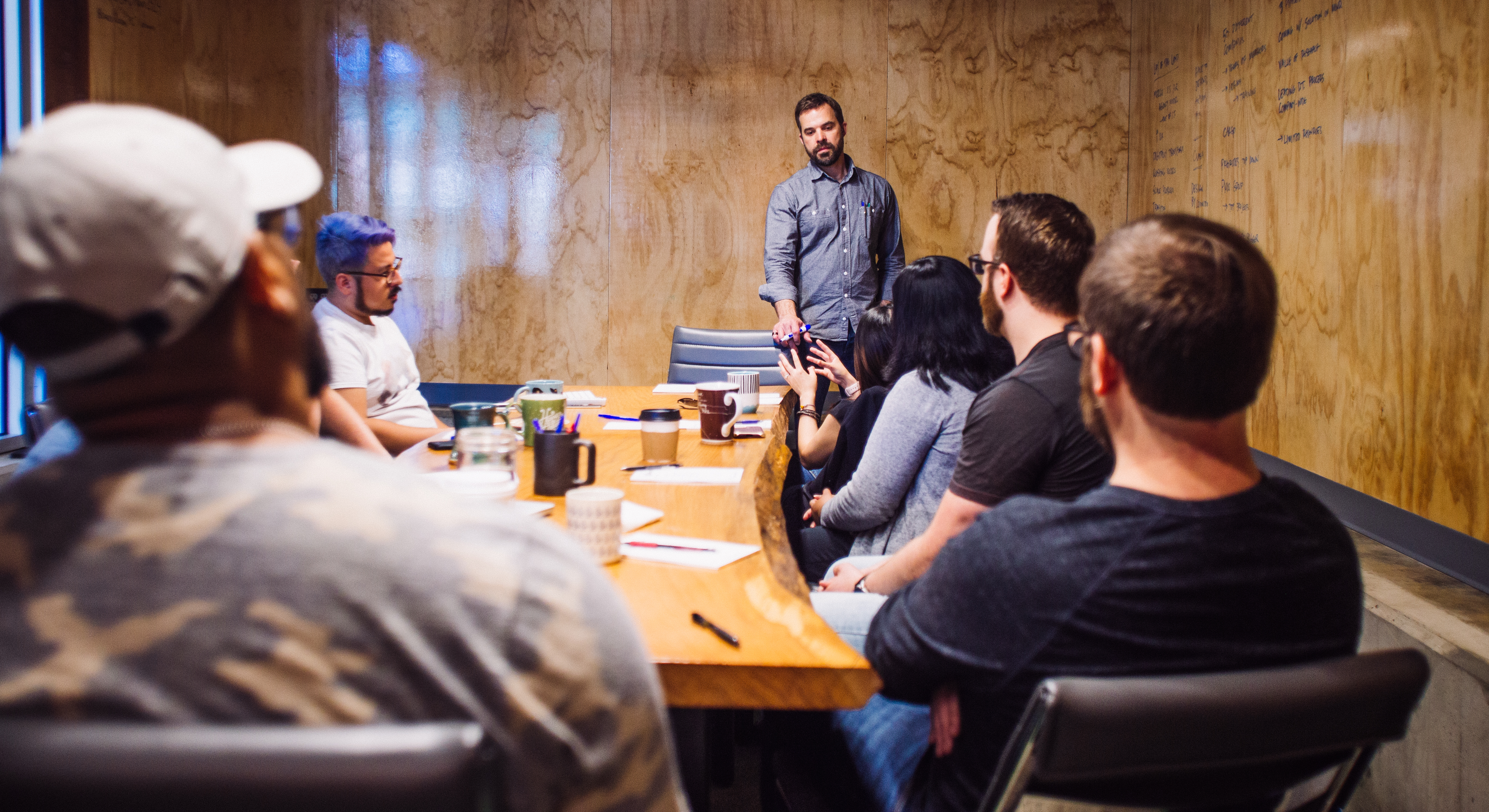 Man leading a workshop standing at the head of a live-edge table as colleagues listen