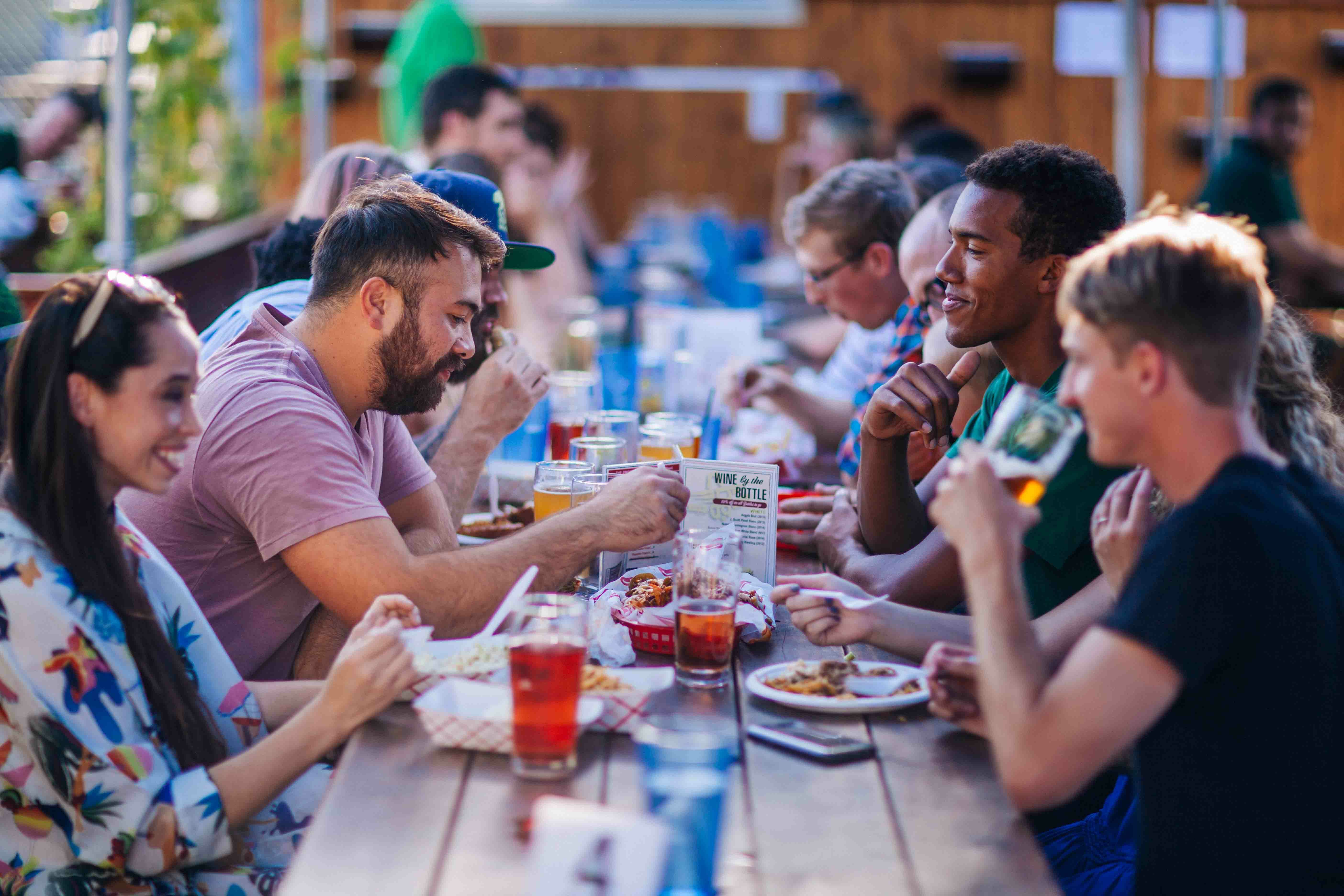 People sharing food and drinks along a long communal table at Beergarden