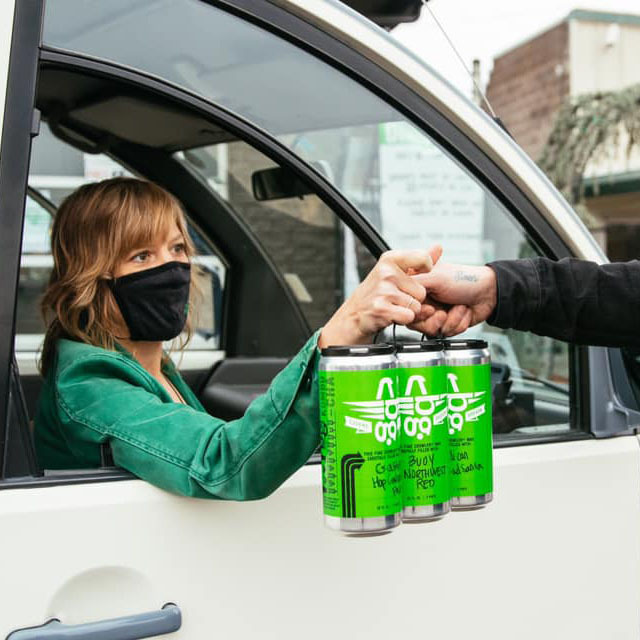 Masked driver handing a green four-pack of Beergarden beer through a car window