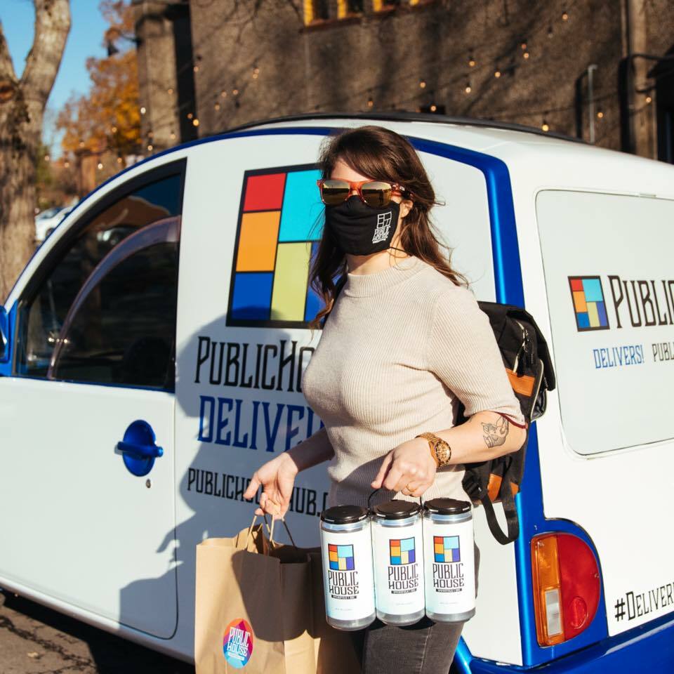 Masked woman carrying Public House crowlers and a bag beside a Public House Delivers van