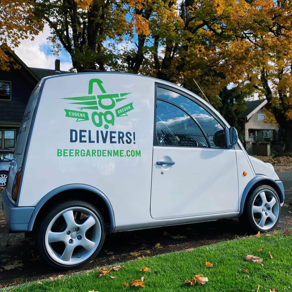 White Beergarden delivery car with snail logo reading BEERGARDENME.COM parked by fall trees