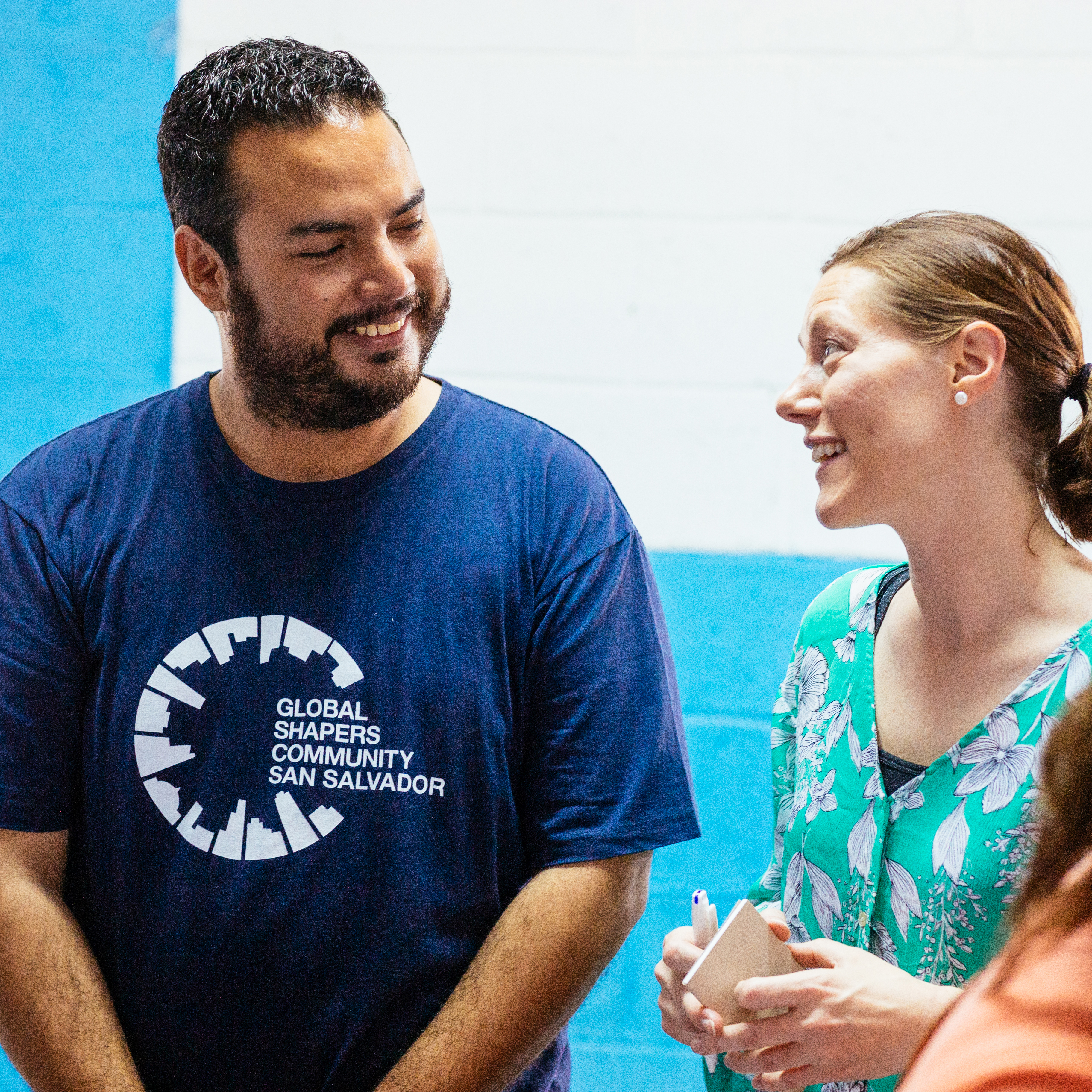 Man in a Global Shapers Community San Salvador tee talking and smiling with a woman in green