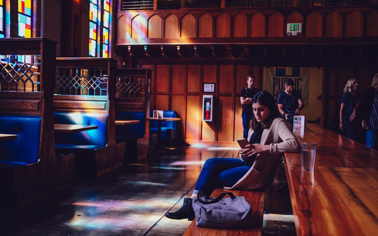Woman on her phone in a converted-church pub with stained glass and wooden booths