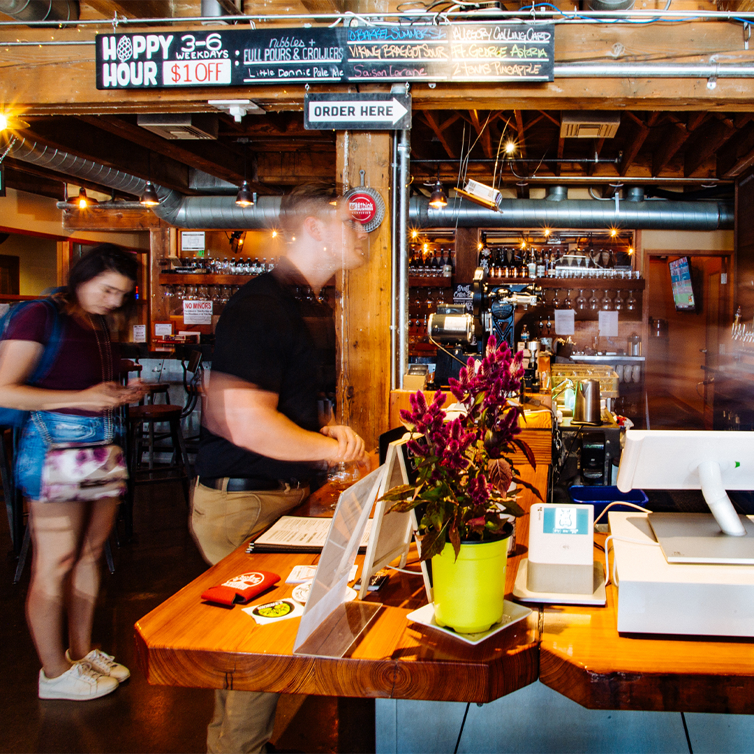 Tap and Growler bar with Happy Hour and Order Here signs, long row of taps and a flower vase