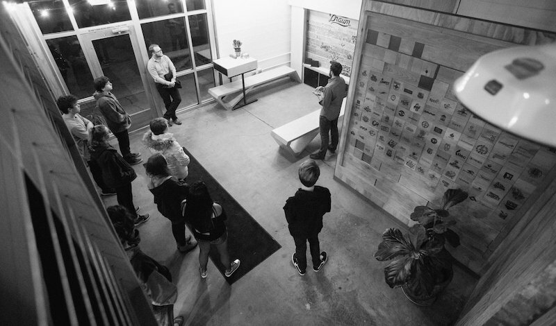 People gathered in the Drawn Bard entryway facing a wall of sample tiles, black-and-white