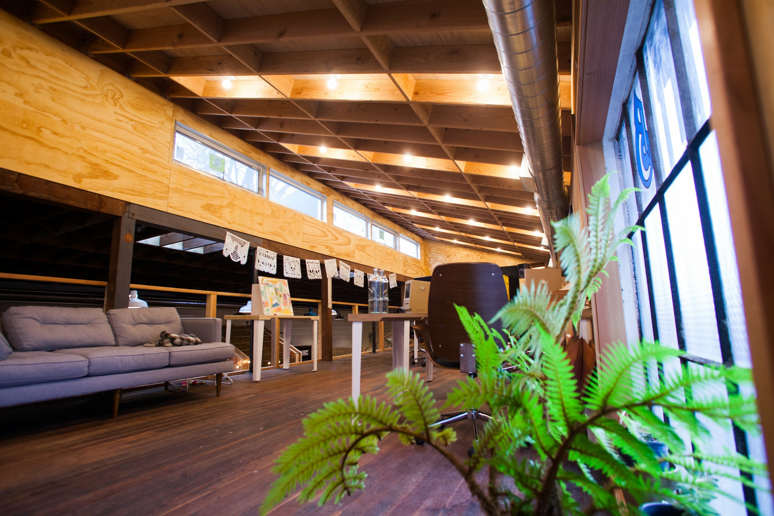 Loft lounge in Drawn's Bard with sofa, wood floors, papel picado banners and a fern
