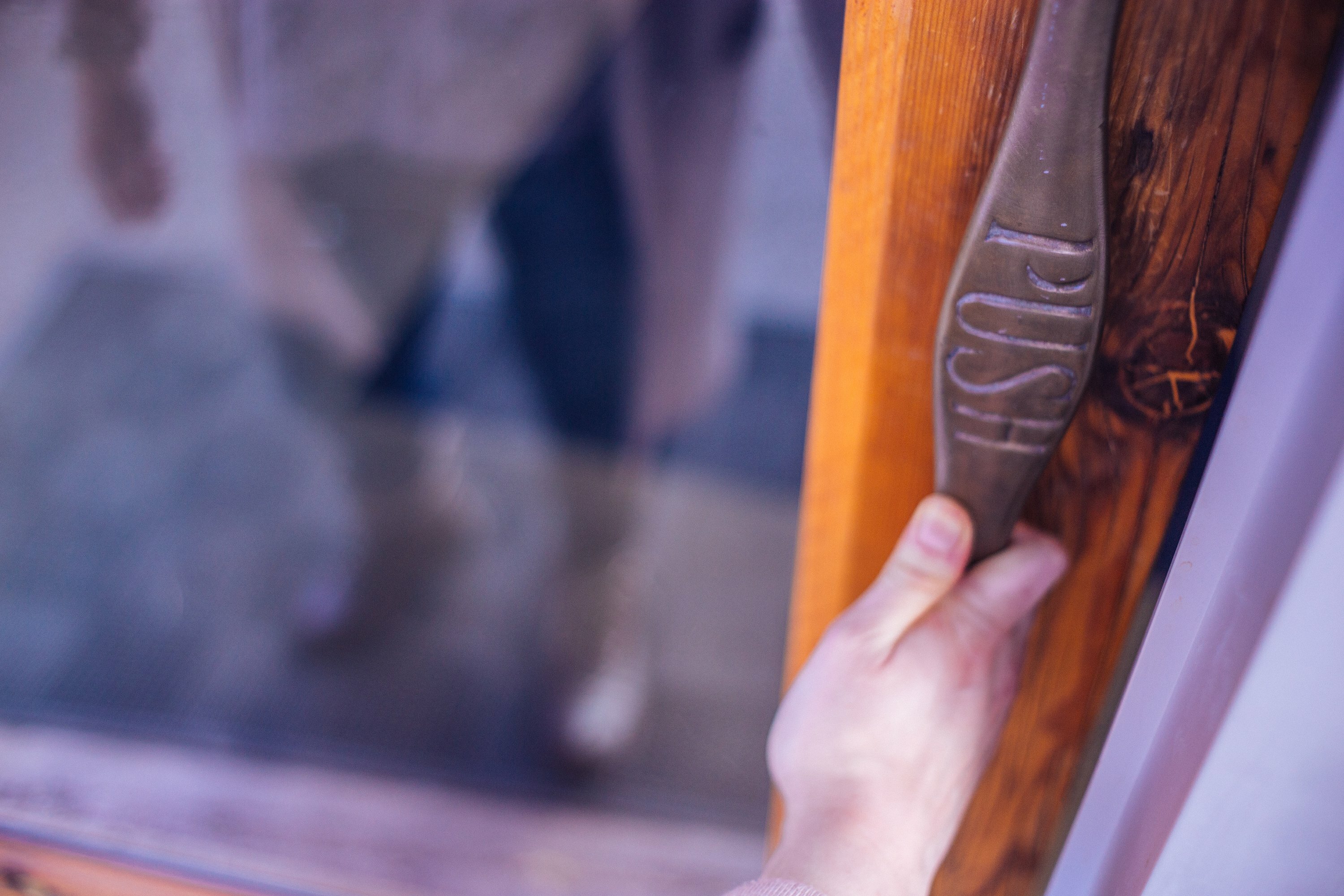 Hand pulling a salvaged wooden door handle carved with the word Push at the Bard