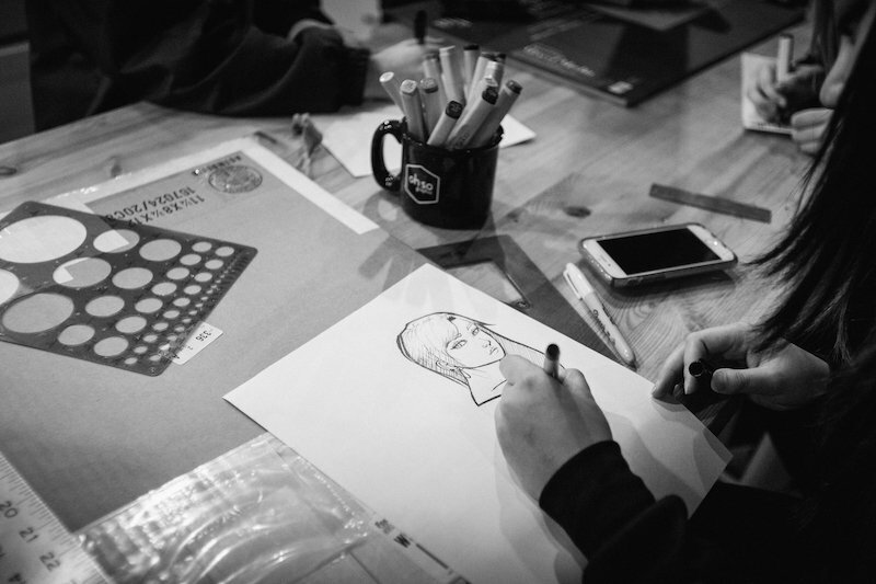 Apprentices and instructor sketching plans around a workbench in a fabrication shop, black-and-white