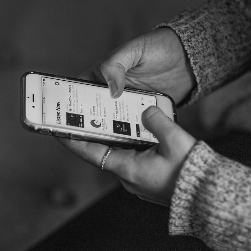 Hands holding a phone showing a podcast app's Listen Now screen, black and white
