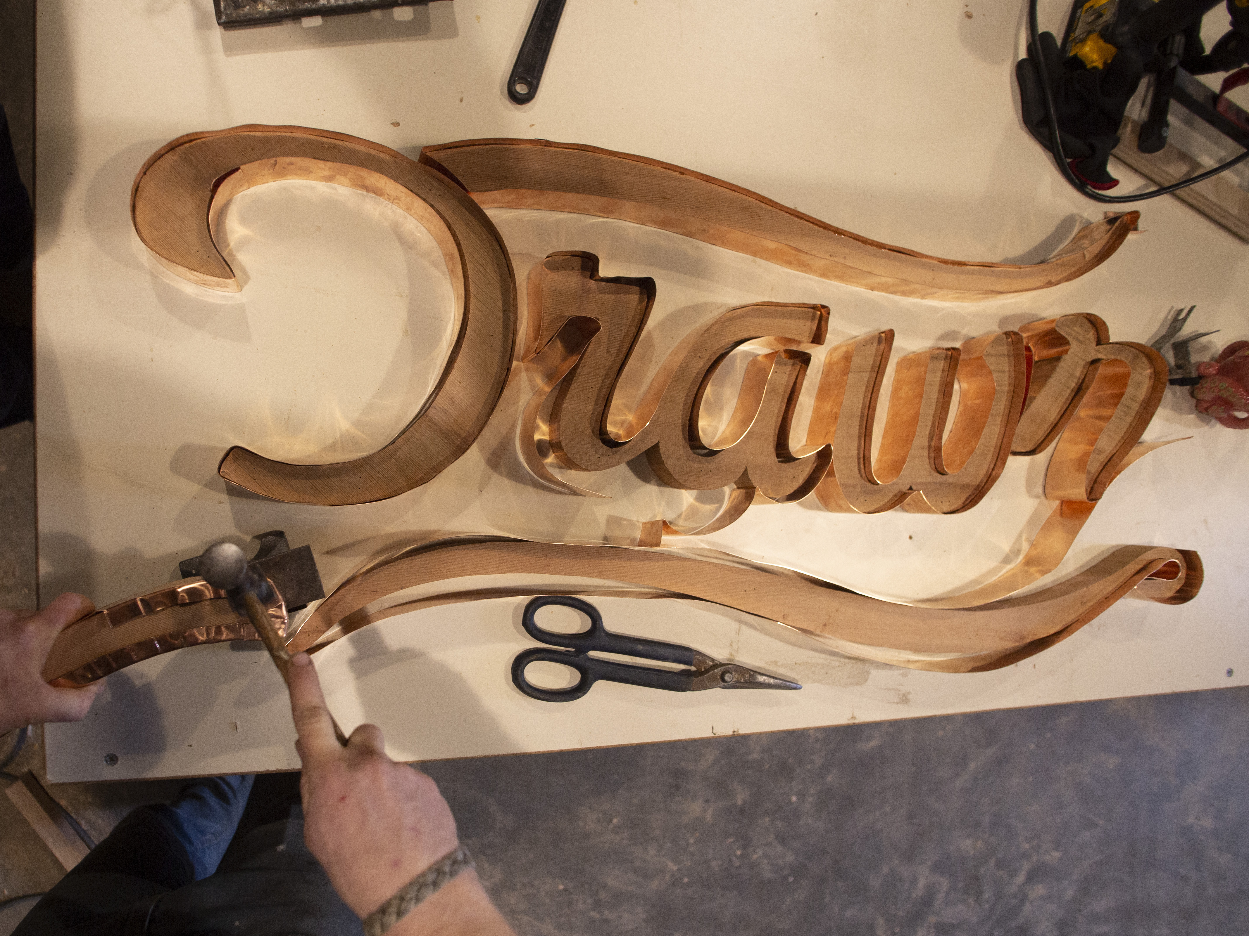 Carved wooden cursive Drawn sign on a workbench with a craftsman's hands and tools