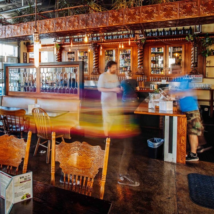 Drawn-designed pub interior with carved wooden chairs, tin ceiling and a backlit bar, patrons moving in long exposure