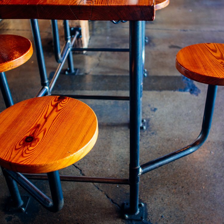 Detail of reclaimed-wood bar stools mounted on black pipe framing over a polished concrete floor