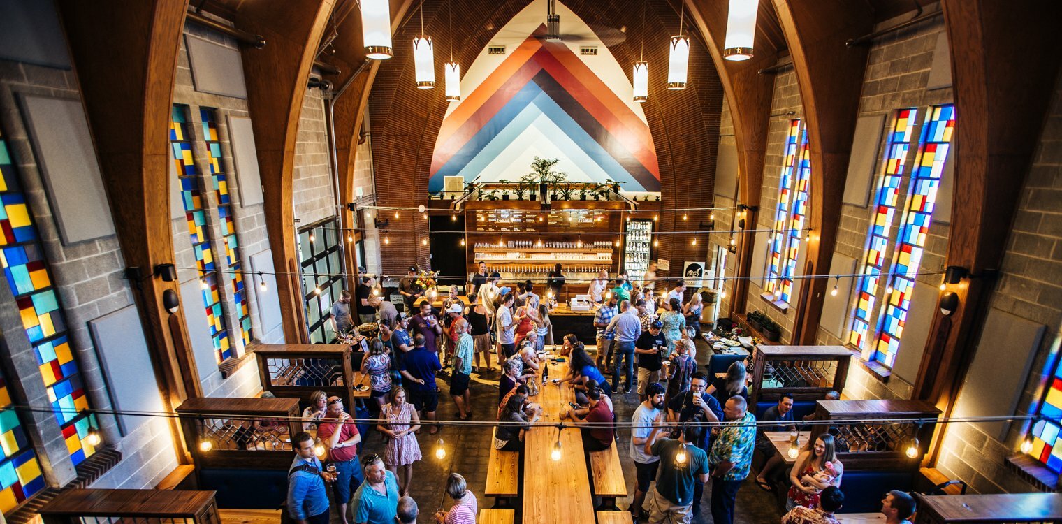 Former church converted to a taproom, arched ceiling and stained-glass windows above a crowd and central bar