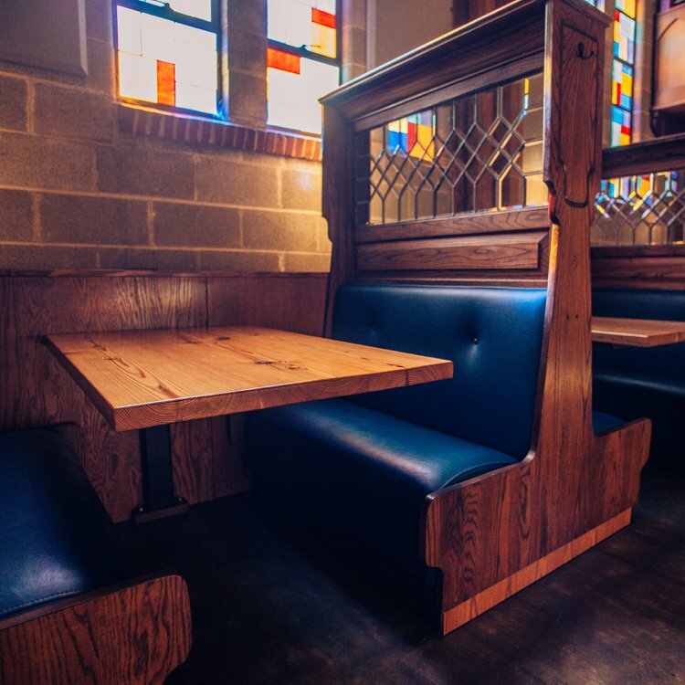 Empty booth with blue leather benches, wood divider and stained-glass window in a church-turned-taproom