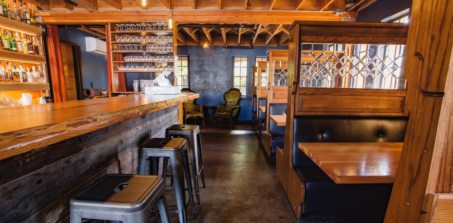 Drawn-designed bar interior with reclaimed-wood counter, metal stools and leather booths beside leaded-glass partitions