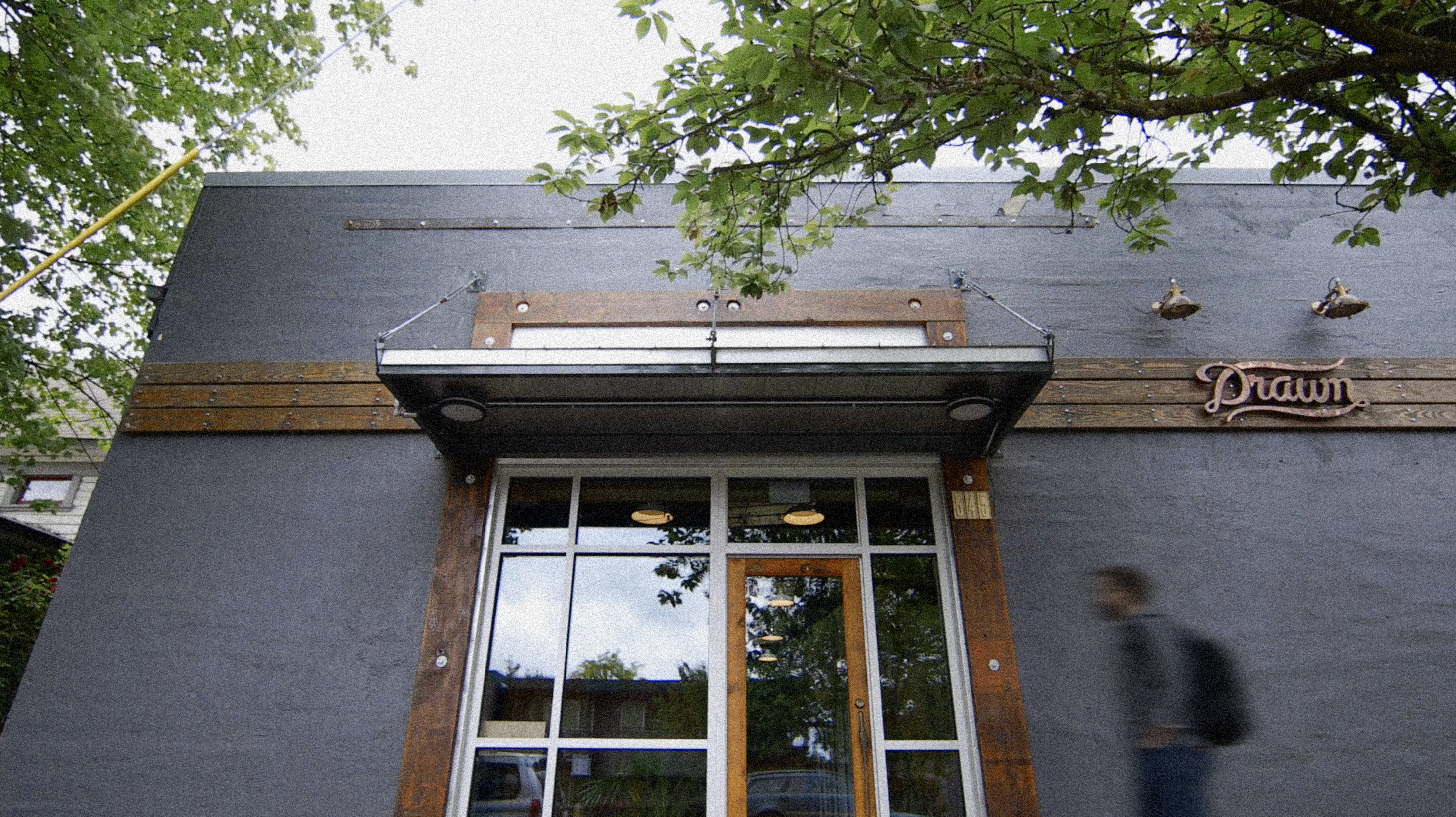 Exterior of the Drawn studio building with script Drawn sign above the entrance and trees overhead