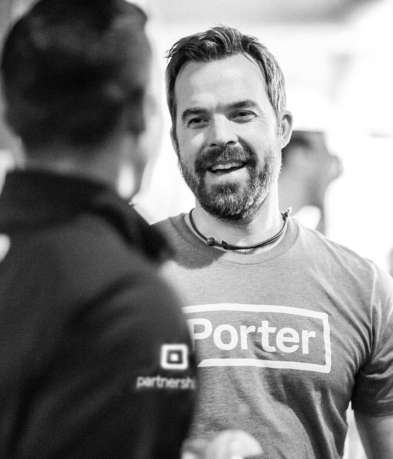 Smiling bearded man in a Porter tee talking with a colleague at an event, black and white