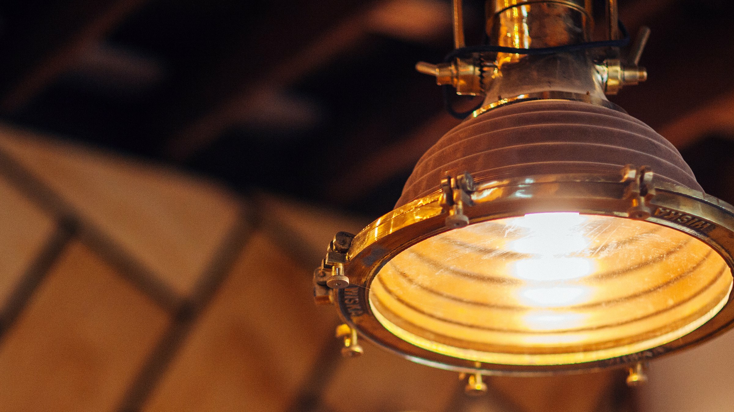 Glowing brass and glass industrial pendant lamp lit against an exposed brick and timber ceiling