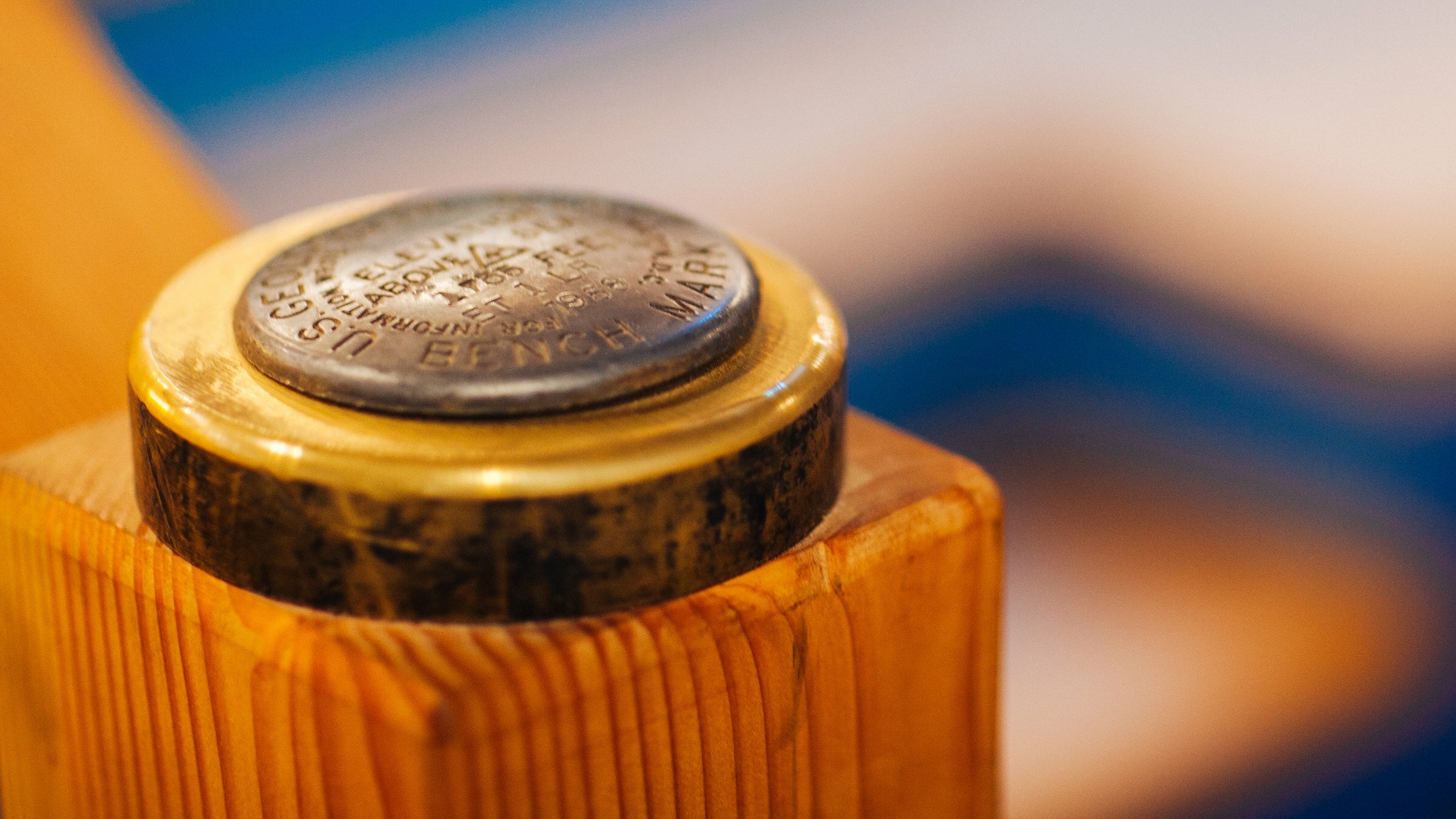 Close-up of the brass Geological Survey elevation marker on a wood post, warm bokeh background