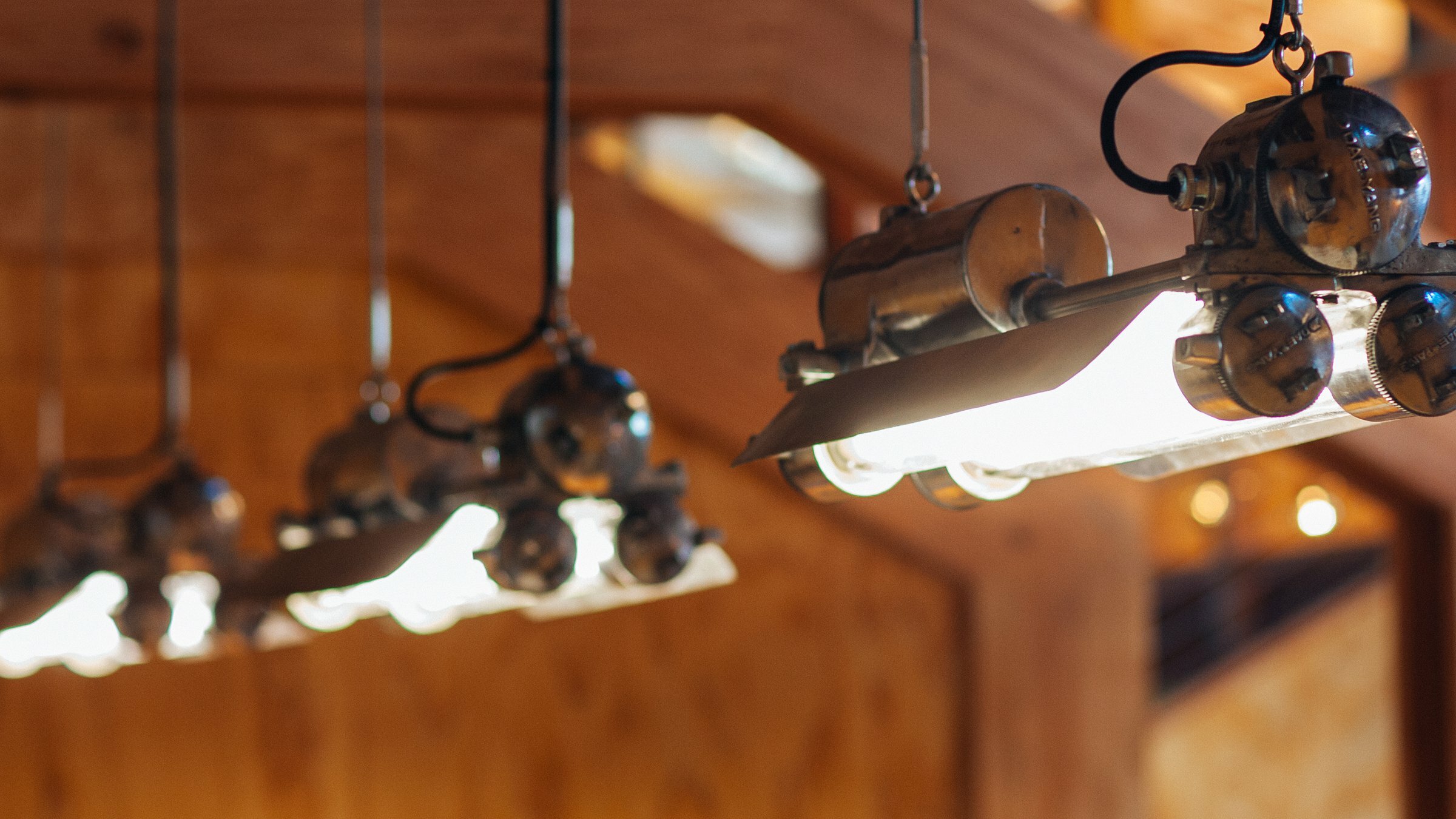 Row of vintage industrial pendant tube lights hanging against warm wood paneling