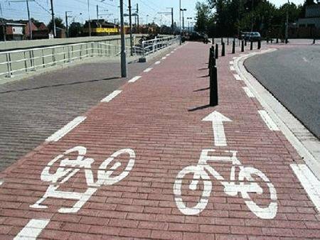 Brick-paved bike lane with painted bicycle symbols and direction arrow beside a road