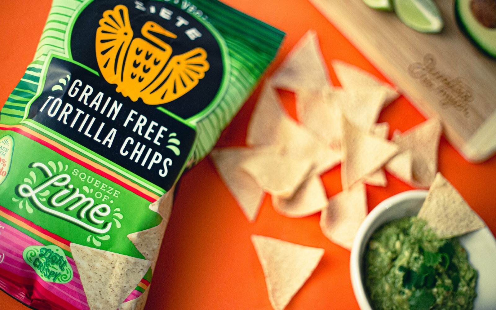 Siete Grain Free Tortilla Chips Squeeze of Lime bag beside scattered chips and guacamole on orange