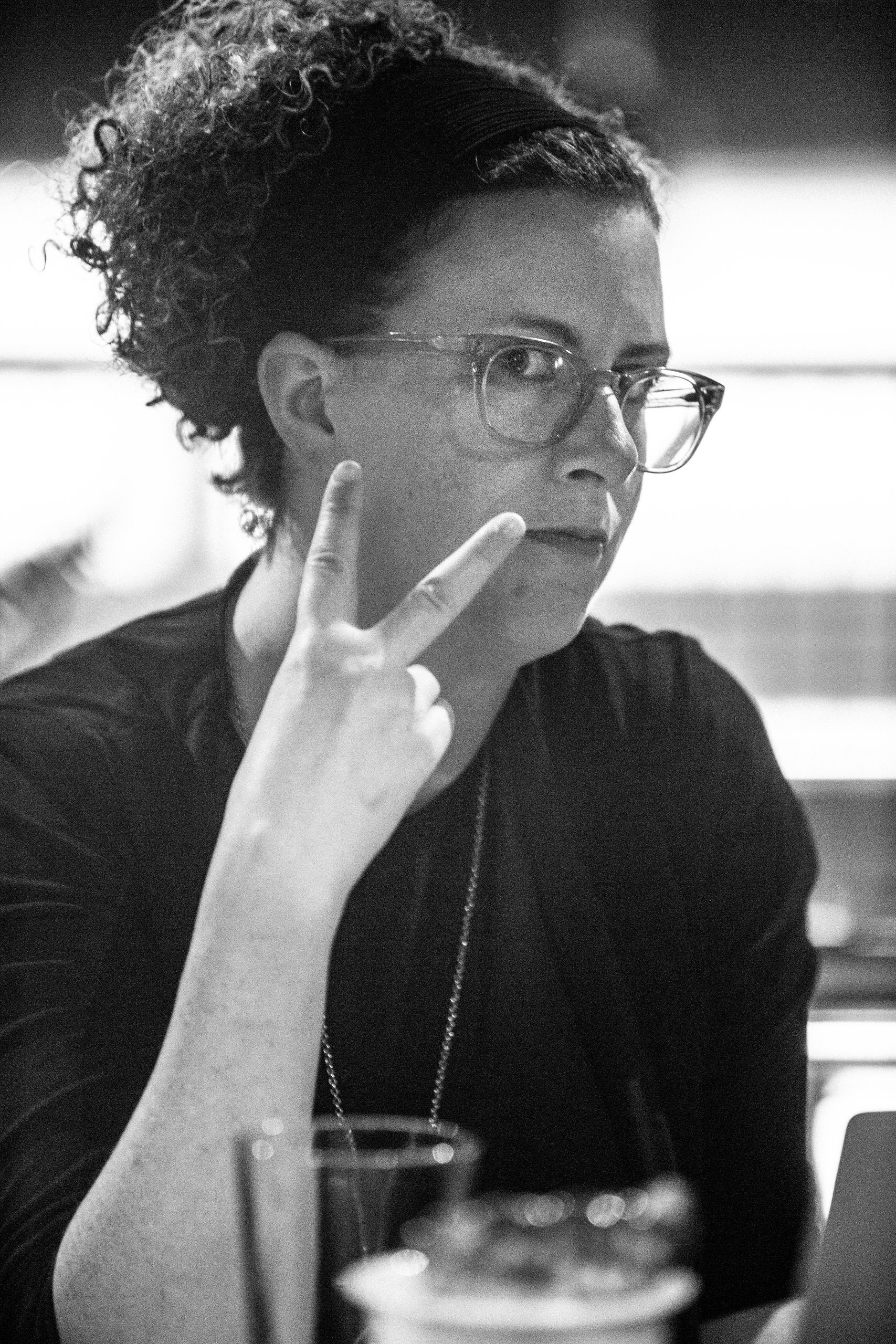 Black-and-white portrait of a woman in glasses gesturing thoughtfully near her face