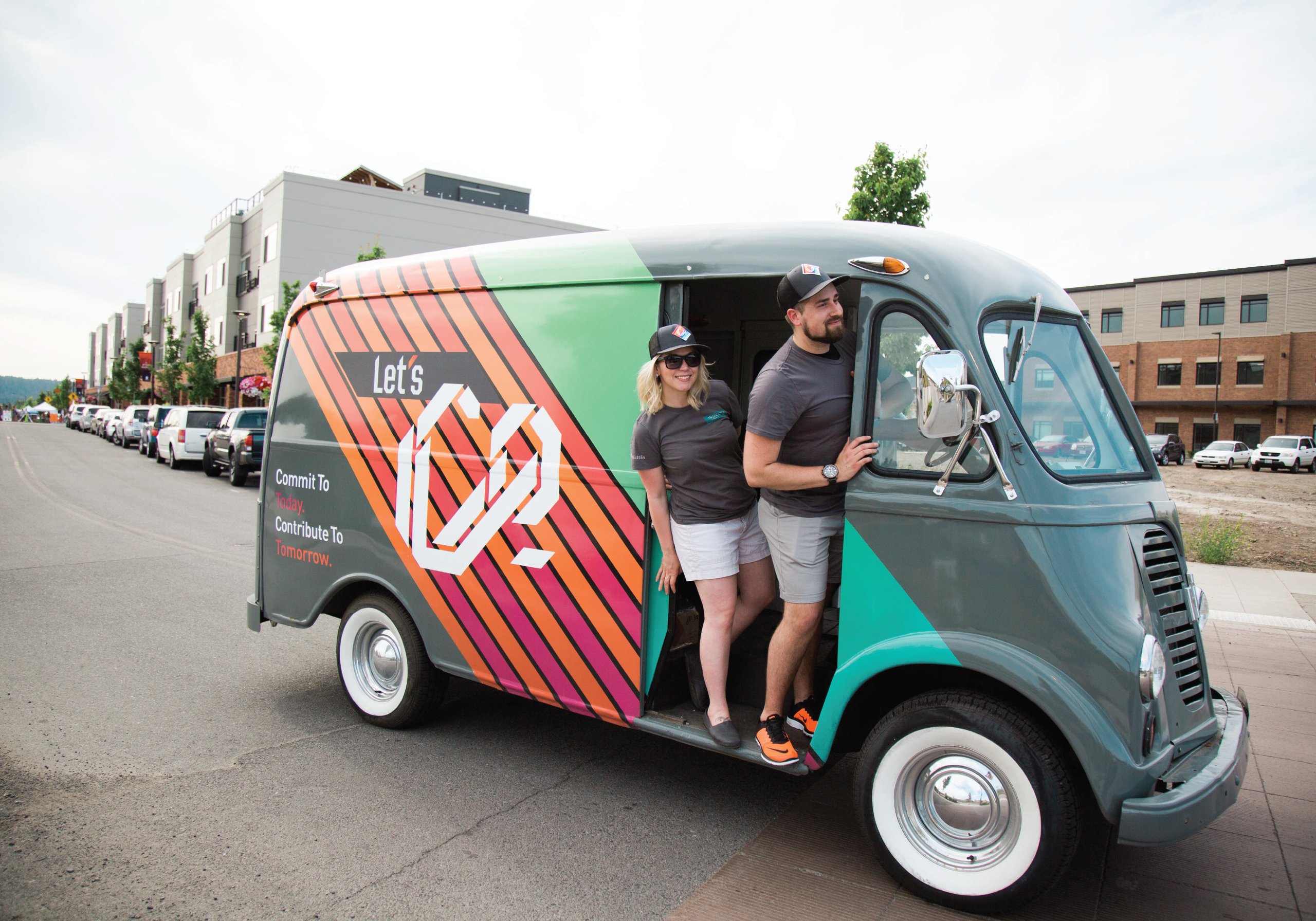 Two people in a vintage van wrapped Let's C2, Commit To Today Contribute To Tomorrow