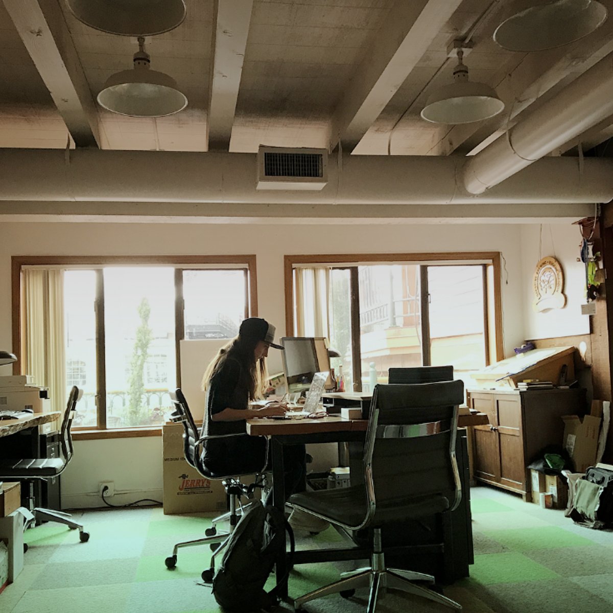 Designer working at a laptop in a sunlit studio with hanging pendant lamps